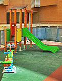 REF 92. Parque infantil. Urbanización PAU 1 en Alicante:
Torre con tobogán pequeño y muelle balancín sobre suelo de caucho rectangular a nivel.
